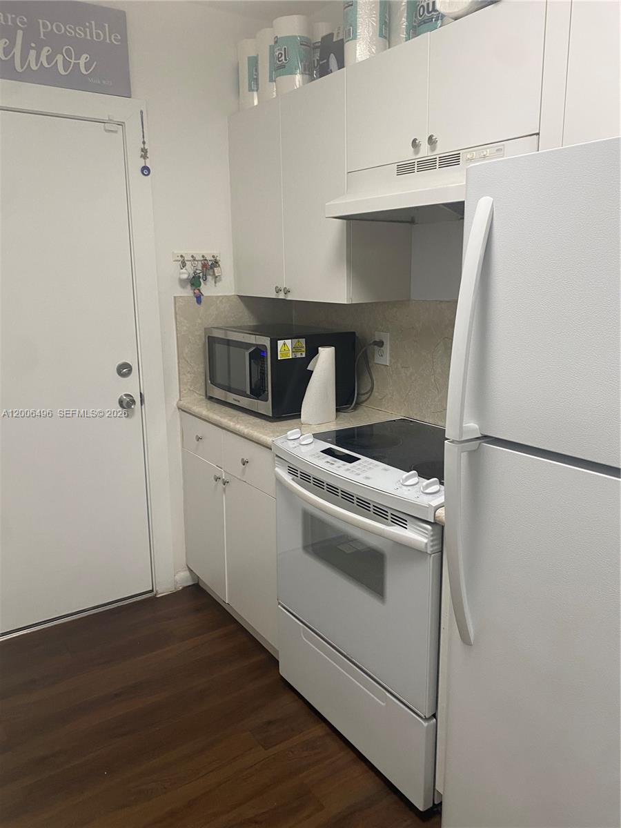 A small kitchen features white cabinets, white appliances, a microwave, and dark wood-look flooring — 900 SW 84th Ave # 415D, Miami FL 33144, MIAMI, FL