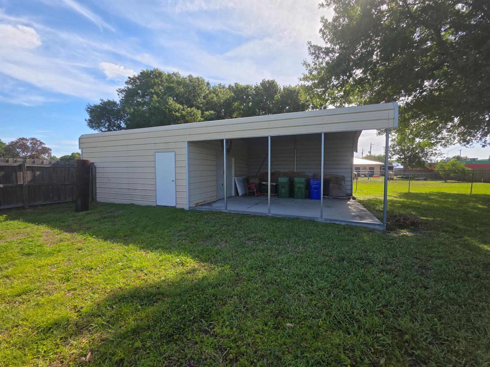 A metal shed with a partially enclosed carport stands on a grassy backyard lawn — 1019 NW 2nd Street, Okeechobee FL 34972, OKEECHOBEE, FL