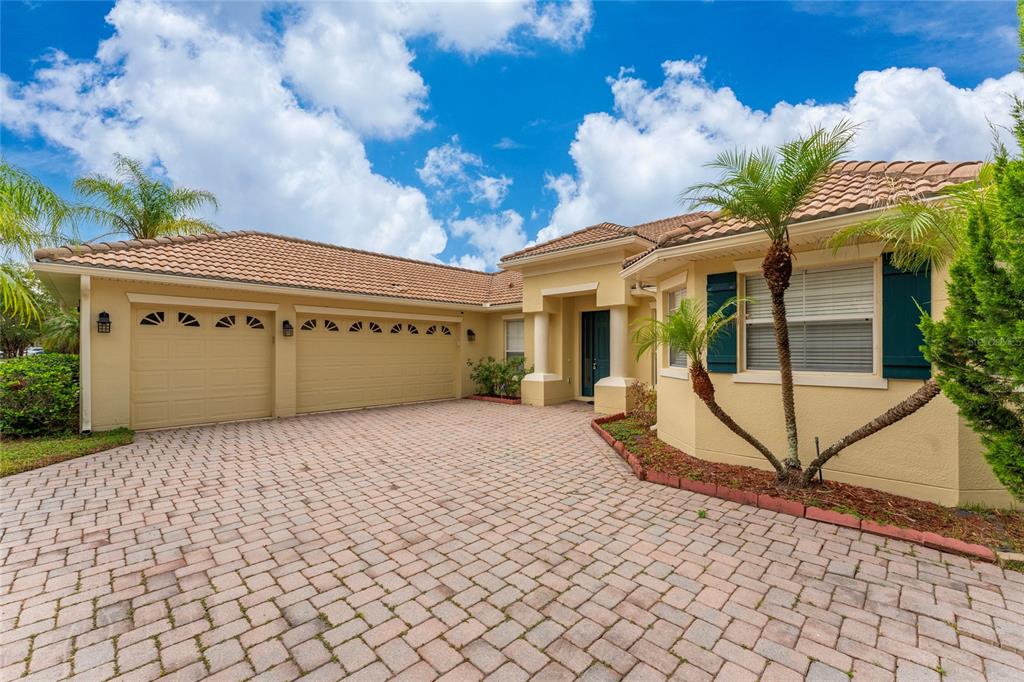 A tan house with a three-car garage and a paved driveway under a blue sky — 3817 GOLDEN FEATHER WAY, KISSIMMEE, FL
