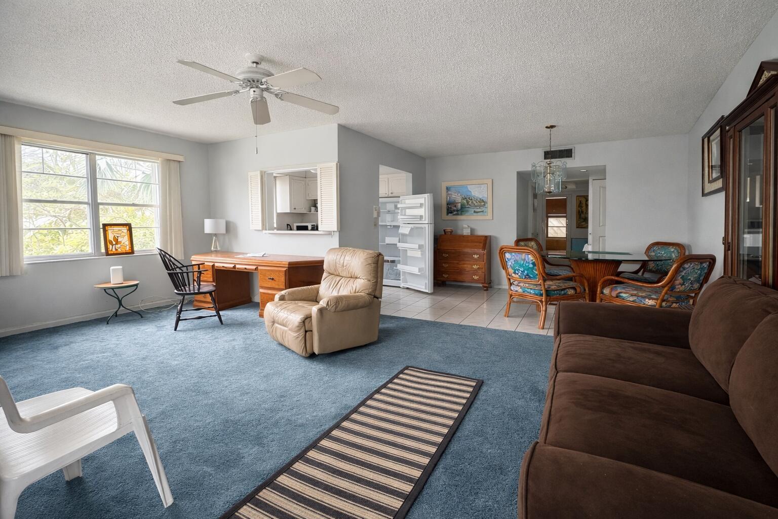 A living room with blue carpeting, a brown sofa, a desk, and a dining area — 315 Tilford O # 315, Deerfield Beach FL 33442, DEERFIELD BEACH, FL