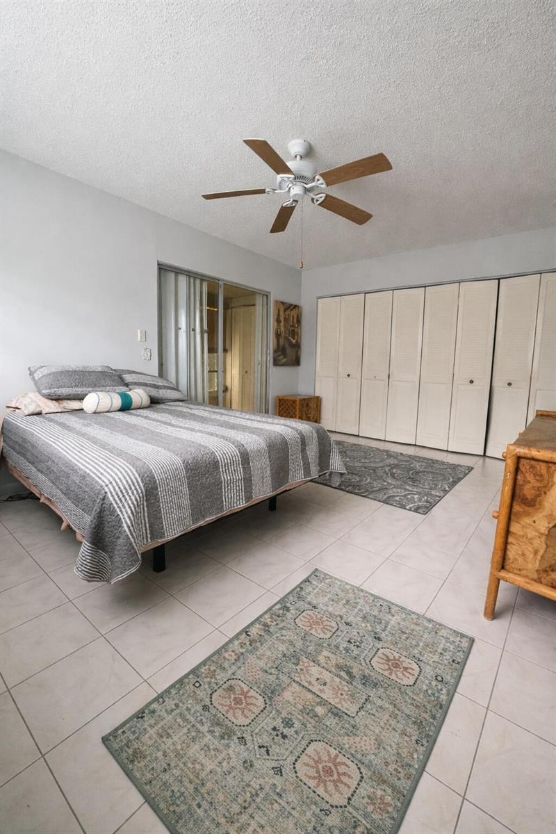 A bedroom features a bed, tiled floors, two area rugs, and a wall of closets — 315 Tilford O # 315, Deerfield Beach FL 33442, DEERFIELD BEACH, FL