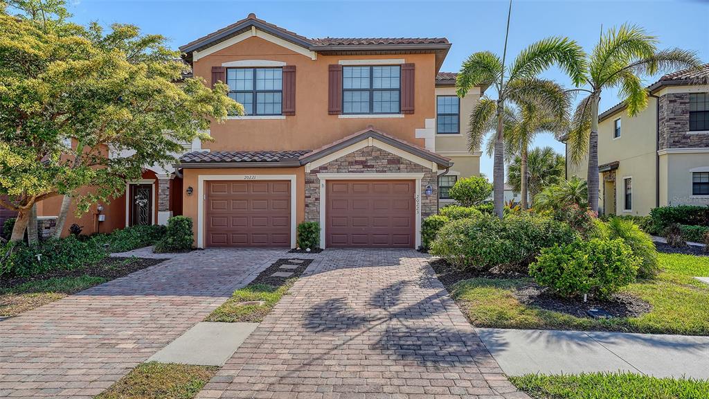A two-story stucco townhouse with a brick paver driveway and two garage doors — 20223 LAGENTE CIRCLE, VENICE, FL