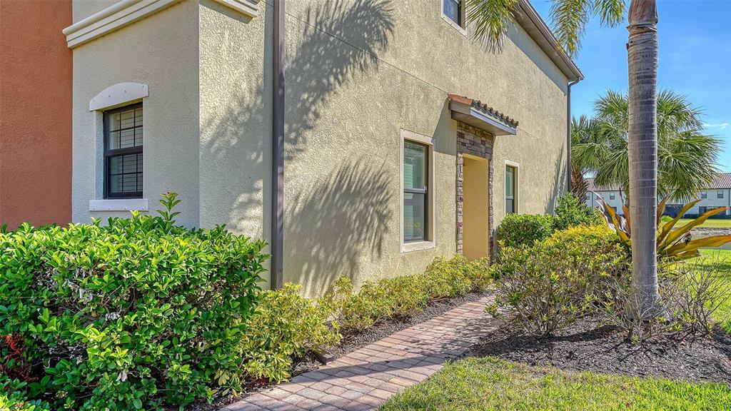 A beige stucco building exterior features a brick walkway leading to a recessed entryway — 20223 LAGENTE CIRCLE, VENICE, FL