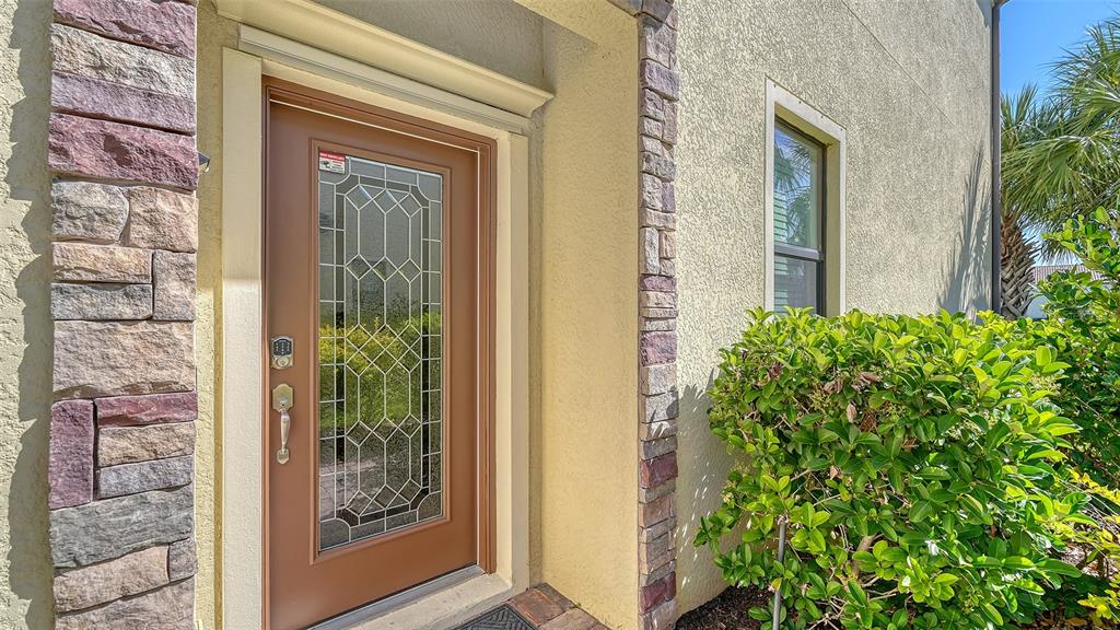 A brown front door with a decorative glass insert sits beside a stone-accented exterior wall — 20223 LAGENTE CIRCLE, VENICE, FL