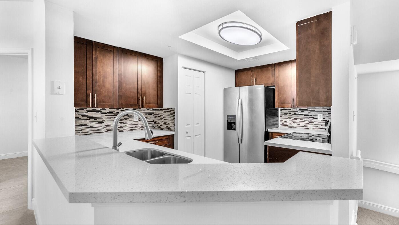 A kitchen features dark wood cabinets, stainless steel appliances, and a light-colored quartz breakfast bar — 20889 Saint Andrews Boulevard, Boca Raton FL 33433, BOCA RATON, FL
