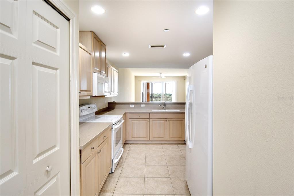 A kitchen with light wood cabinets, white appliances, and tile flooring opens to a living area — 1921 MONTE CARLO DRIVE UNIT 603, SARASOTA, FL