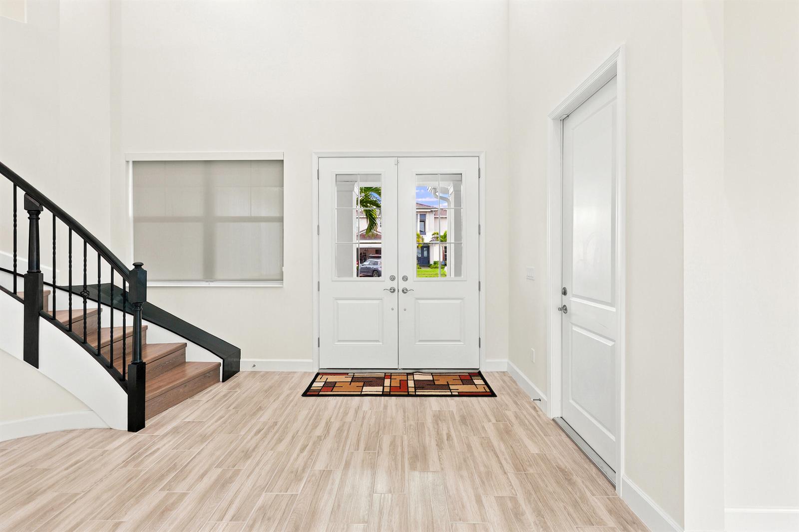 An entryway features a double front door, a staircase with black railings, and light flooring — 5627 Opal Drive, FL 33470, FL