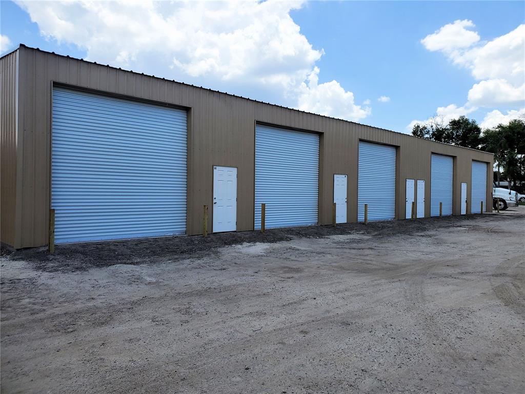 A long, tan metal storage building features multiple roll-up garage doors and white entry doors — 532 N BLUFORD AVENUE, OCOEE, FL