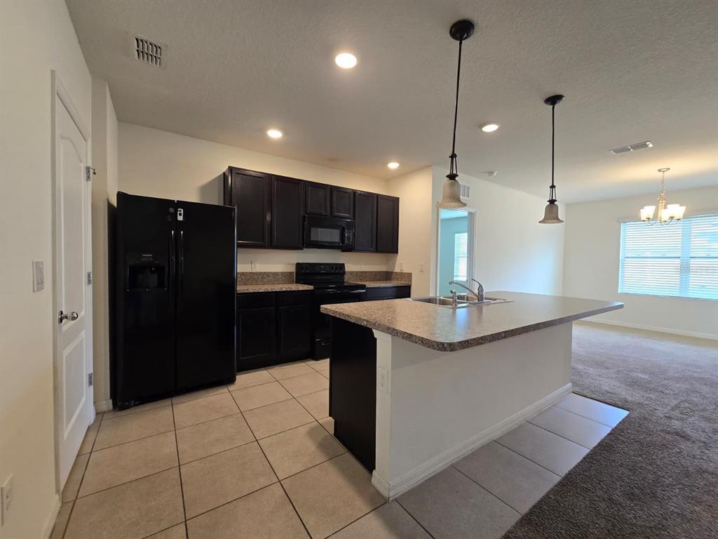 A kitchen features dark cabinets, black appliances, a granite-topped island, and light-colored tile flooring — 1895 CASSIDY KNOLL DRIVE, KISSIMMEE, FL