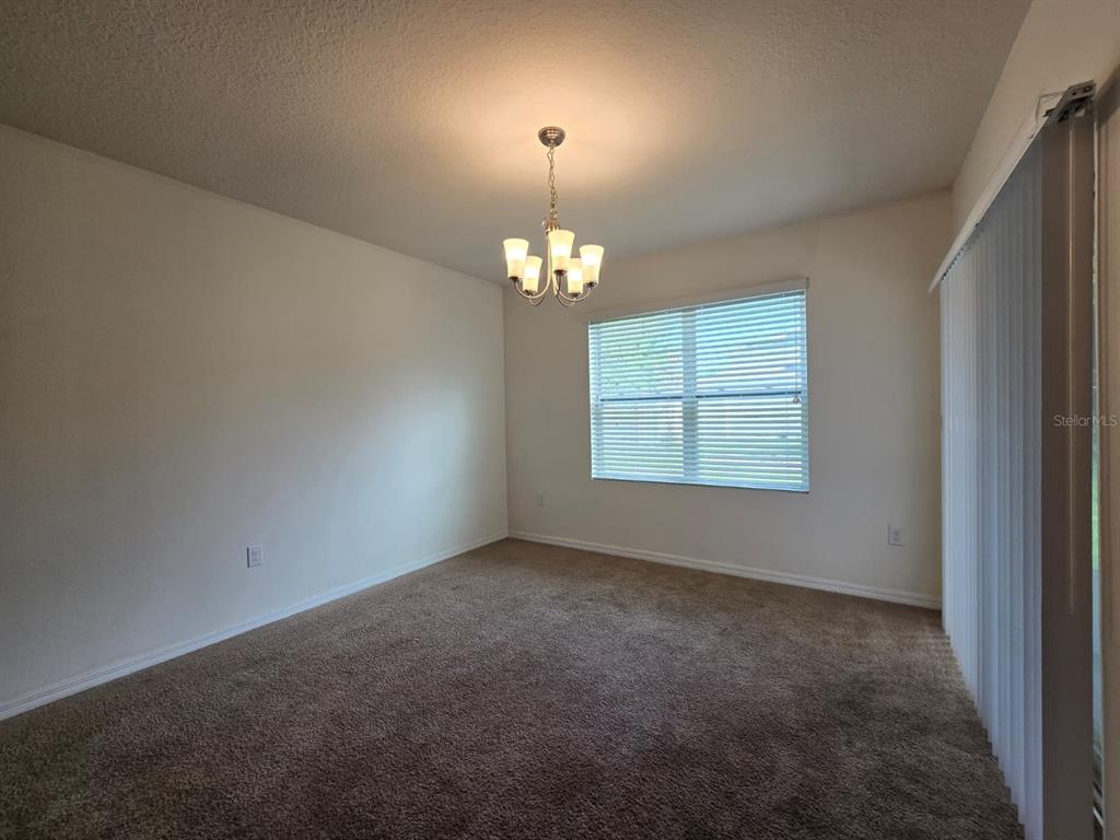 An empty room with beige carpet, a chandelier, a window with blinds, and sliding doors — 1895 CASSIDY KNOLL DRIVE, KISSIMMEE, FL