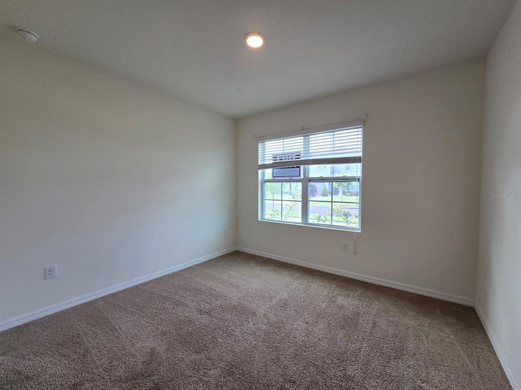 An empty bedroom features beige walls, brown carpet, and a window with white blinds — 1895 CASSIDY KNOLL DRIVE, KISSIMMEE, FL