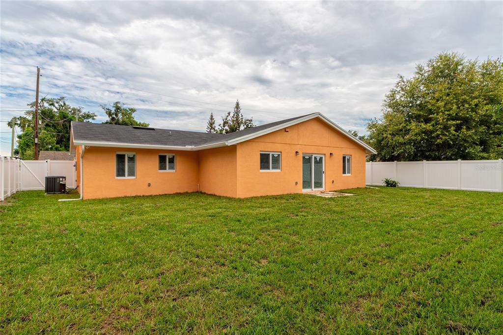 The back exterior of an orange house features a lawn, white fencing, and sliding doors — 1015 MACK AVENUE, ORLANDO, FL