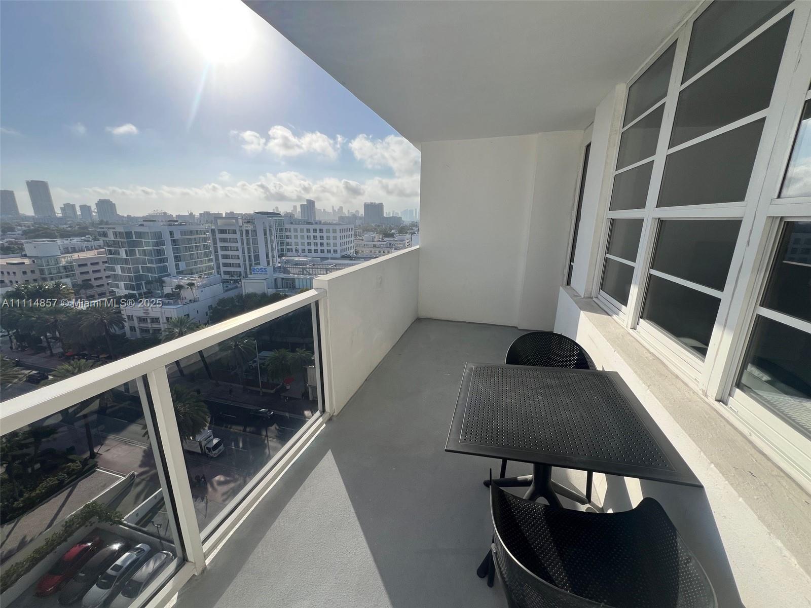 A balcony with a small table and two chairs overlooks a city skyline — 100 Lincoln Rd # 1207, Miami Beach FL 33139, MIAMI BEACH, FL