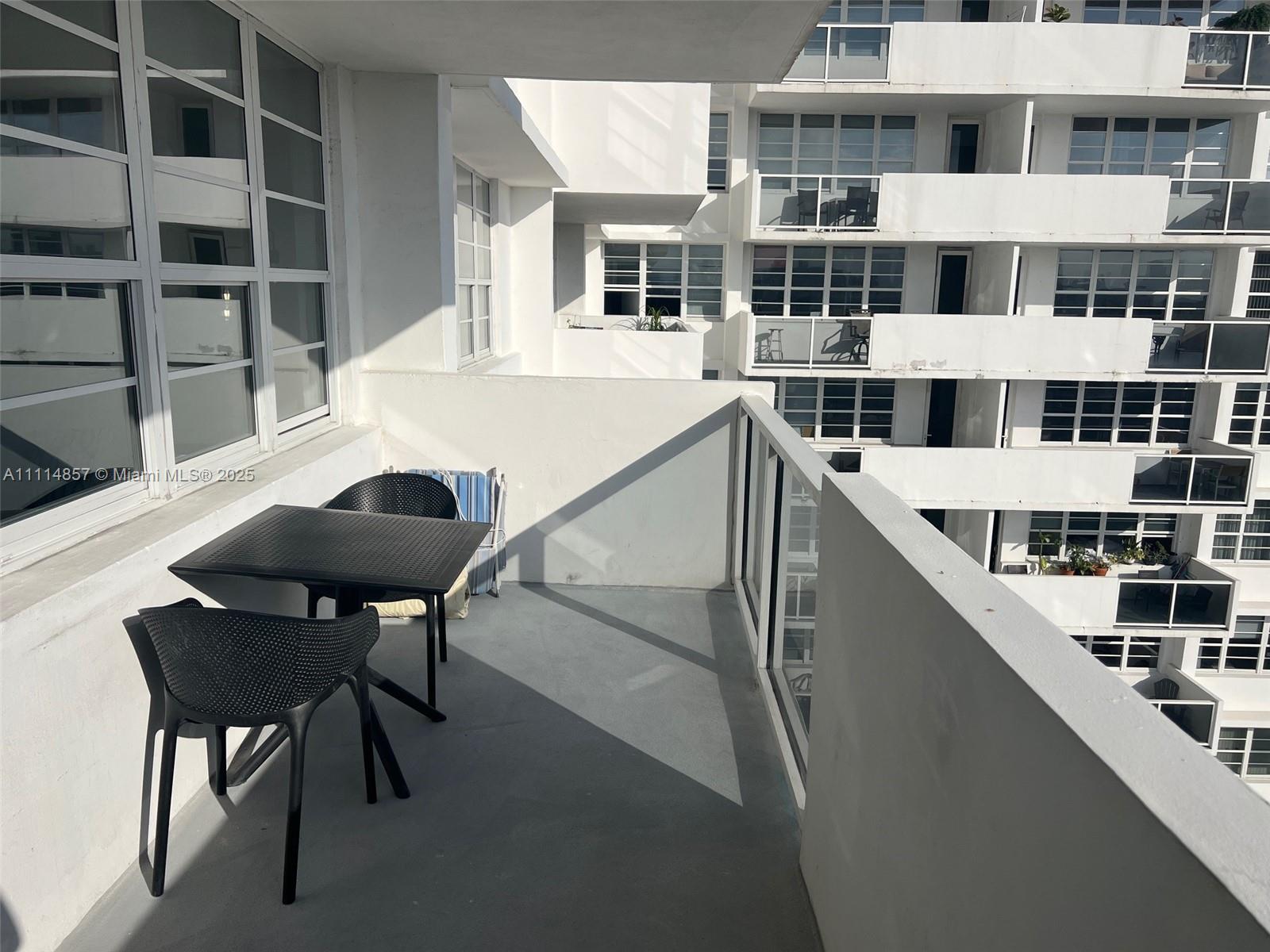 A balcony with a small table and two chairs overlooks a neighboring apartment building — 100 Lincoln Rd # 1207, Miami Beach FL 33139, MIAMI BEACH, FL