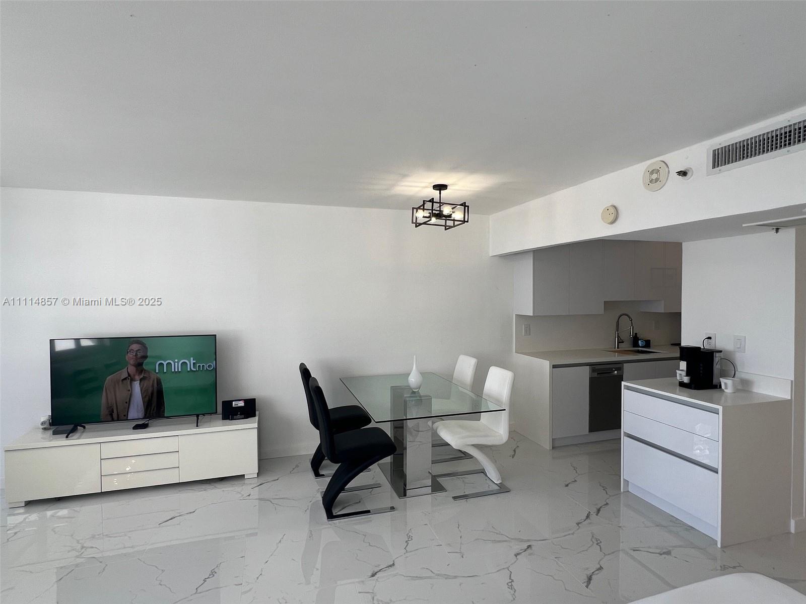 A modern open-concept living and dining area features white marble floors and a glass table — 100 Lincoln Rd # 1207, Miami Beach FL 33139, MIAMI BEACH, FL