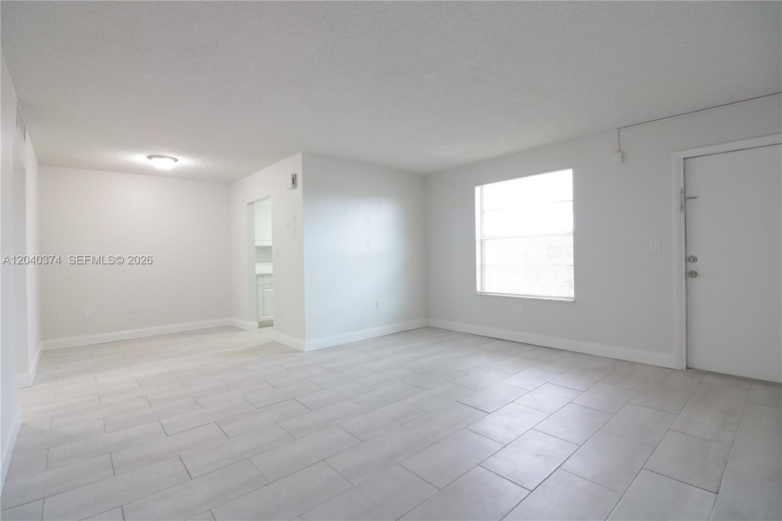 An empty living room features white walls, light-colored tile flooring, and a single window — 400 NE 1st St # 108, Hallandale Beach FL 33009, HALLANDALE BEACH, FL