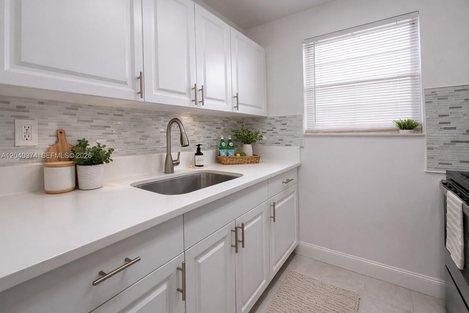 A kitchen features white cabinets, a stainless steel sink, and a gray tiled backsplash — 400 NE 1st St # 108, Hallandale Beach FL 33009, HALLANDALE BEACH, FL