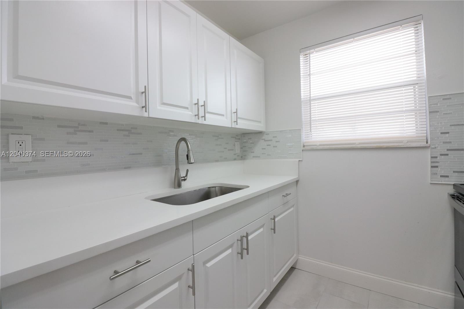 A white kitchen features shaker-style cabinets, a stainless steel sink, and a glass tile backsplash — 400 NE 1st St # 108, Hallandale Beach FL 33009, HALLANDALE BEACH, FL