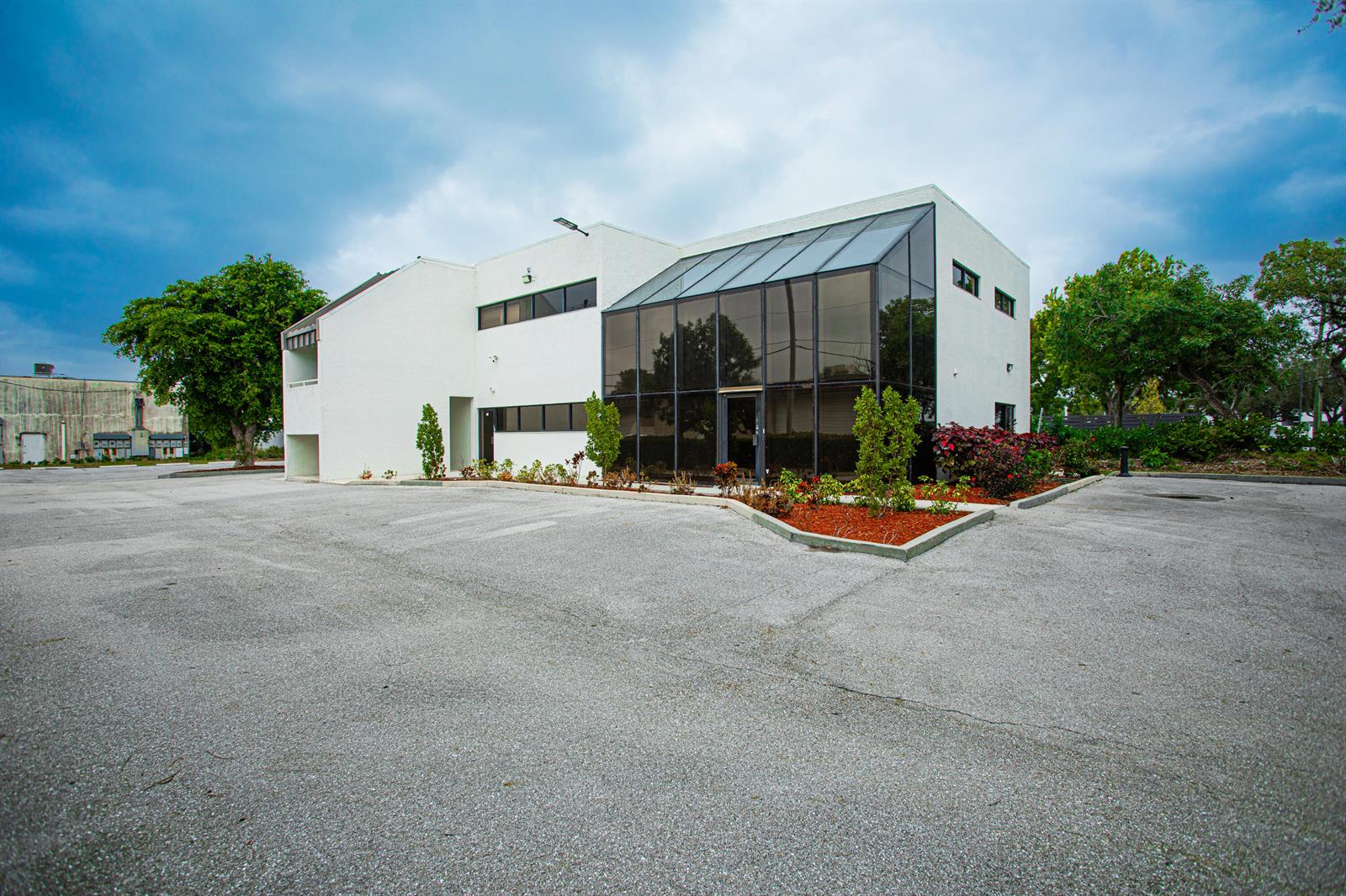 A two-story white commercial building with a glass-enclosed atrium and a large paved parking lot — 1700 Okeechobee Road, West Palm Beach FL 33409, WEST PALM BEACH, FL