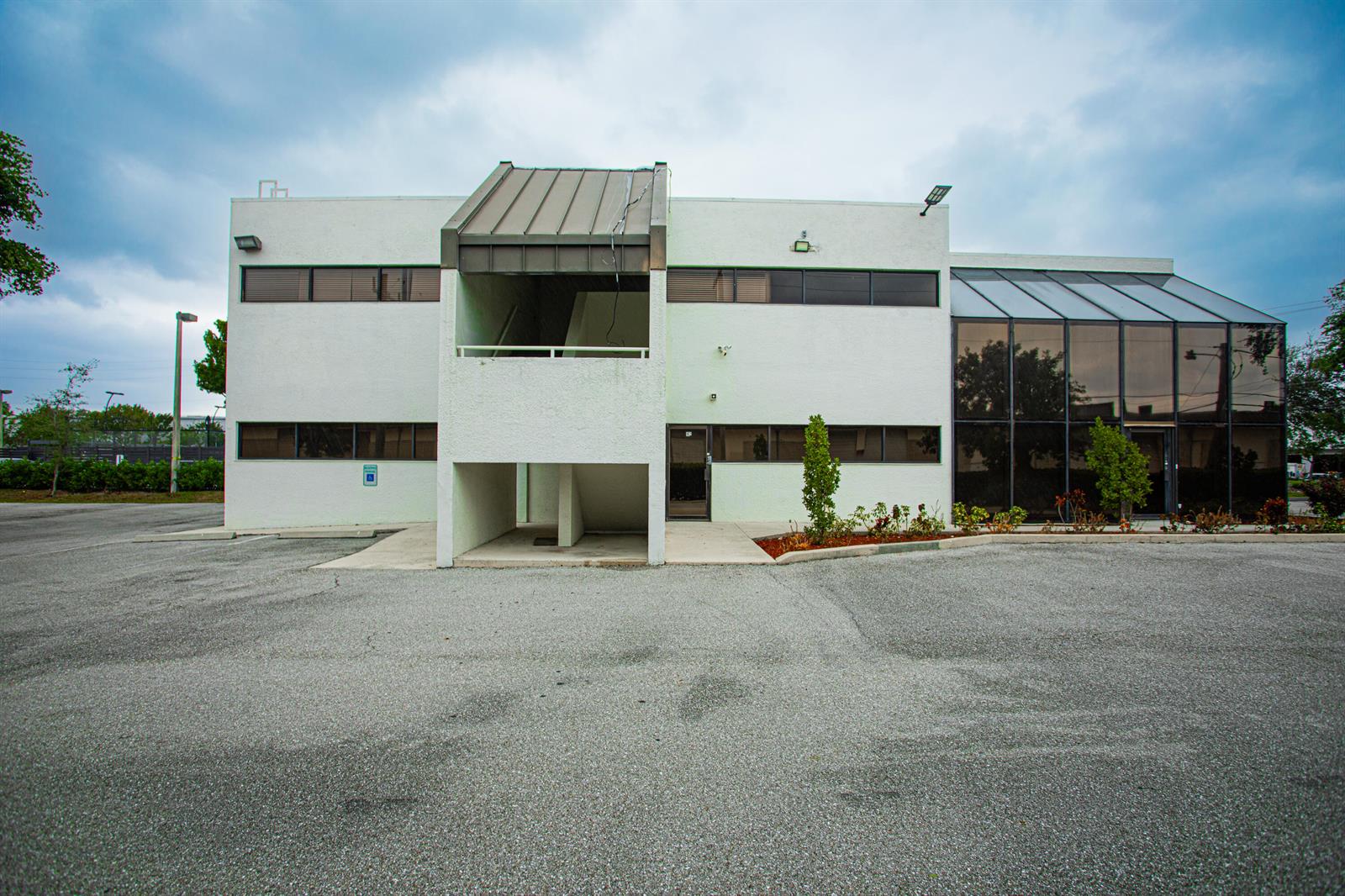 A two-story commercial building with a white stucco facade, dark windows, and a glass atrium — 1700 Okeechobee Road, West Palm Beach FL 33409, WEST PALM BEACH, FL