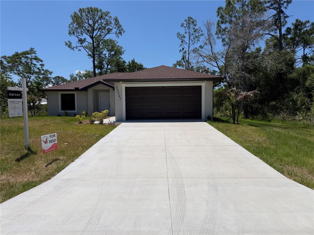 A single-story house with a concrete driveway, a two-car garage, and a for-sale sign — 23367 MAYVILLE AVENUE, PUNTA GORDA, FL