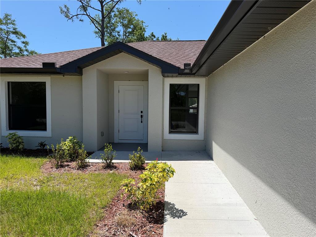 The exterior of a house features a white front door, a concrete walkway, and landscaping — 23367 MAYVILLE AVENUE, PUNTA GORDA, FL