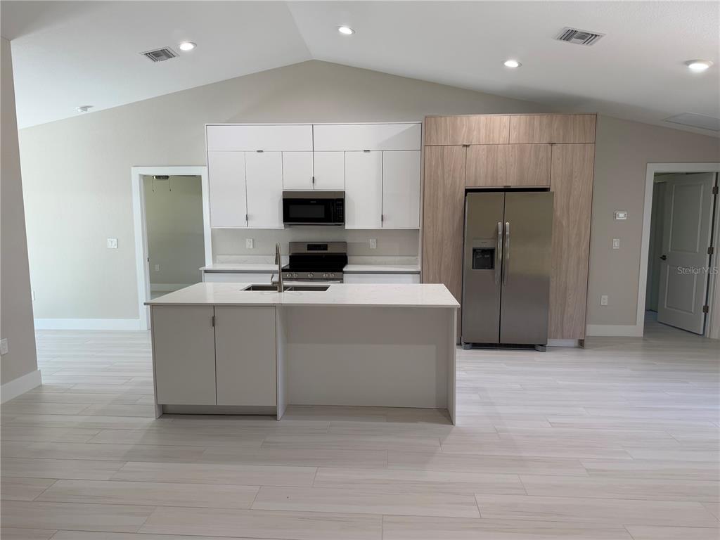A modern kitchen features white cabinets, a wood-paneled refrigerator wall, and a central island — 23367 MAYVILLE AVENUE, PUNTA GORDA, FL