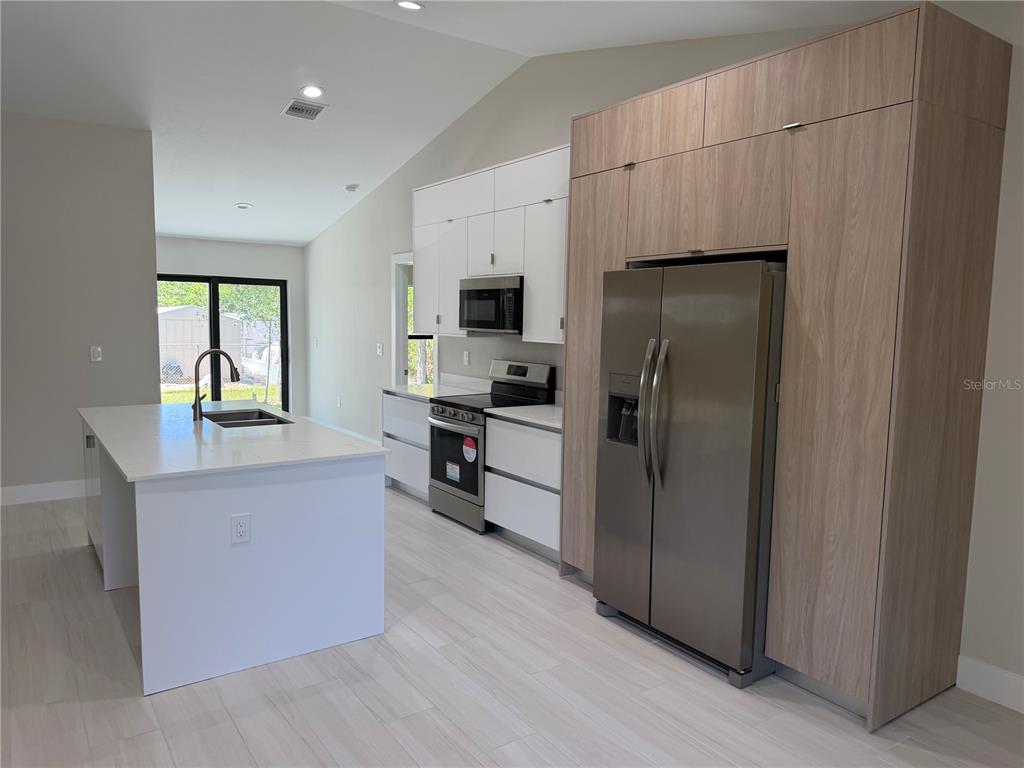A modern kitchen features white cabinets, a wood-paneled refrigerator enclosure, and a central island — 23367 MAYVILLE AVENUE, PUNTA GORDA, FL