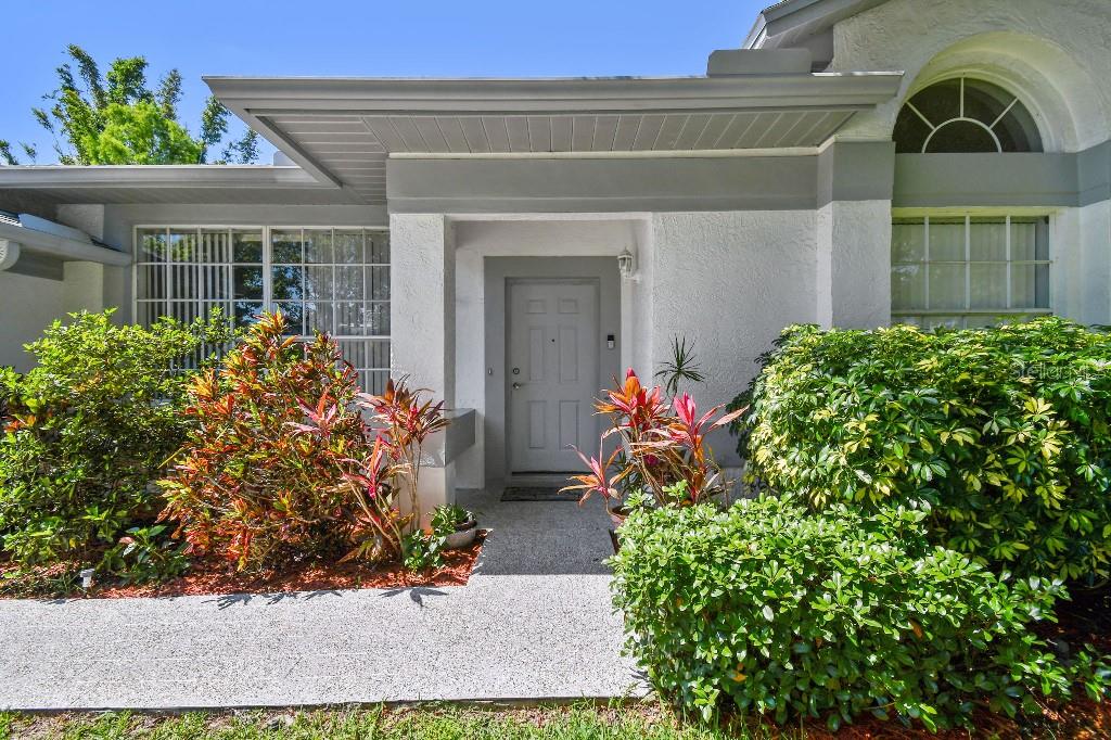 The exterior of a house features a gray front door, large windows, and lush landscaping — 915 BRITTANY PARK BOULEVARD, TARPON SPRINGS, FL