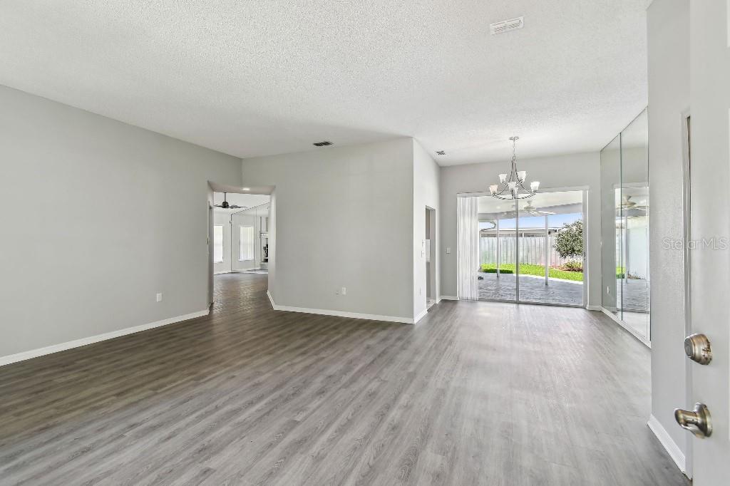 An open-concept living and dining area features gray wood-look flooring, light walls, and sliding glass doors — 915 BRITTANY PARK BOULEVARD, TARPON SPRINGS, FL