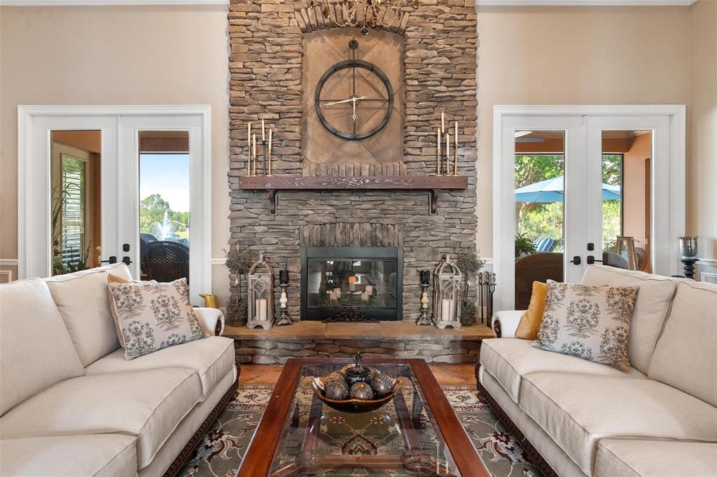 A living room features a stone fireplace, a large wall clock, and two beige sofas — 3001 ISOLA BELLA BOULEVARD, MOUNT DORA, FL