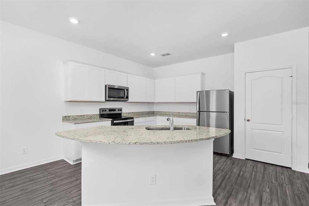 A kitchen with white cabinets, granite countertops, stainless steel appliances, and wood-look flooring — 556 BAY LEAF DRIVE, POINCIANA, FL