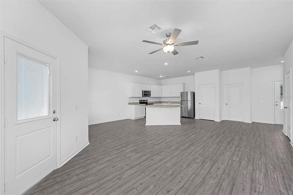 An open-concept kitchen and living area features white cabinets, stainless appliances, and gray flooring — 556 BAY LEAF DRIVE, POINCIANA, FL