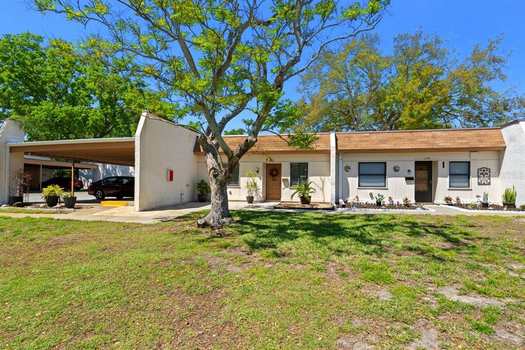 A single-story residential building with a carport, tan siding, and a large tree in front — 1276 MISSION CIRCLE UNIT 45A, CLEARWATER, FL