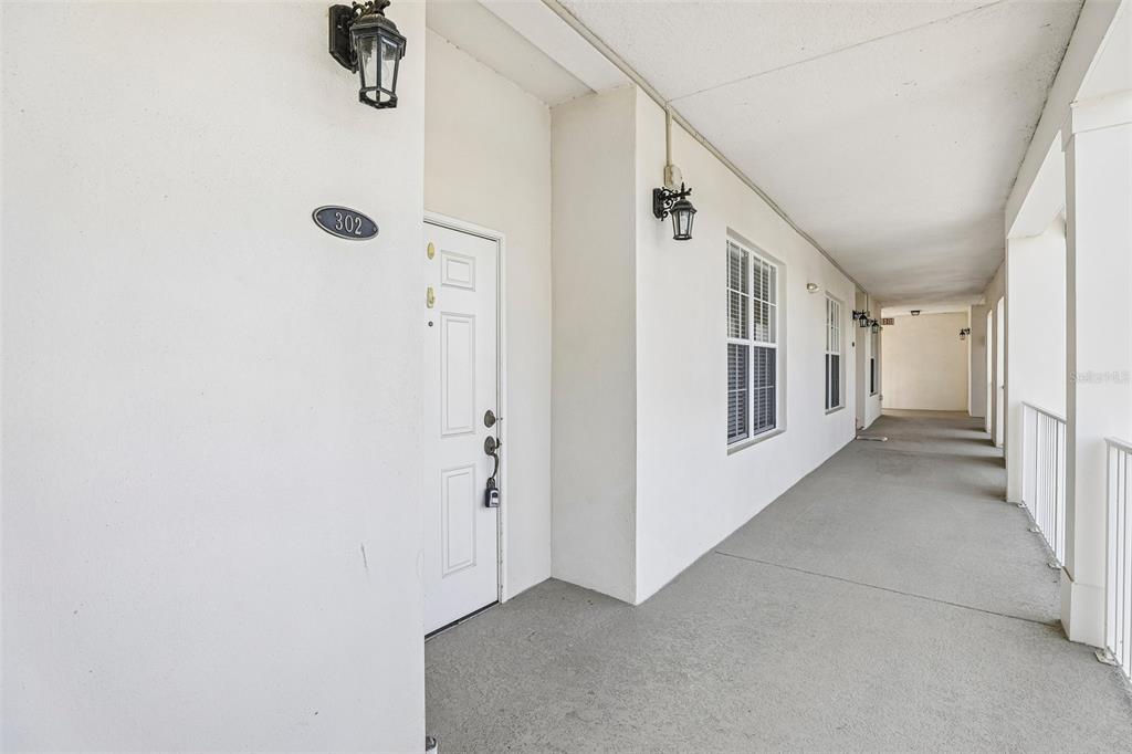 An exterior view of a white apartment building hallway with unit 302 — 2315 UPPER PARK ROAD UNIT 302, ORLANDO, FL
