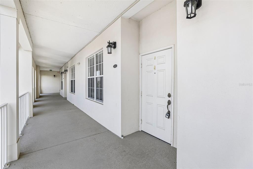A white exterior door opens onto a long, covered concrete walkway with wall-mounted light fixtures — 2315 UPPER PARK ROAD UNIT 302, ORLANDO, FL
