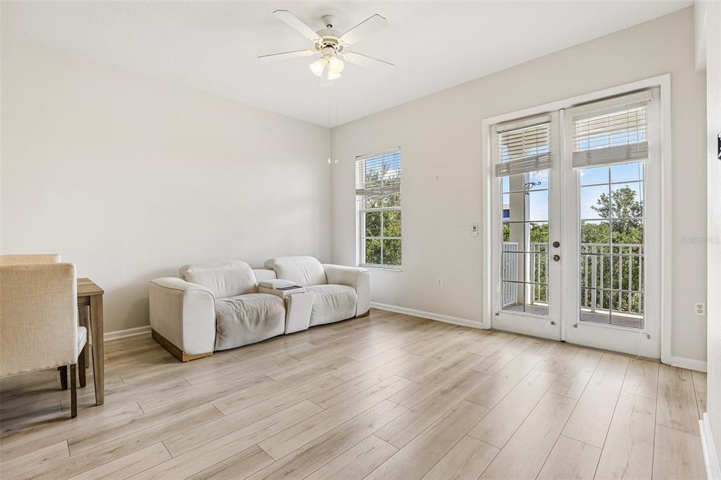 A living room with light wood flooring, a white sofa, and glass doors to a balcony — 2315 UPPER PARK ROAD UNIT 302, ORLANDO, FL