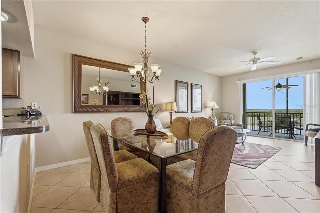 A dining area with a glass table and upholstered chairs opens to a living room — 7705 GRAND ESTUARY TRAIL UNIT 305, BRADENTON, FL