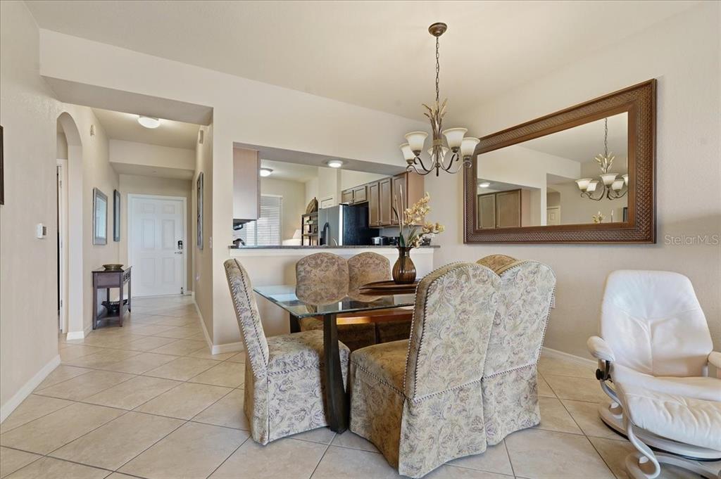 A dining area features a glass-topped table, upholstered chairs, a chandelier, and a wall mirror — 7705 GRAND ESTUARY TRAIL UNIT 305, BRADENTON, FL