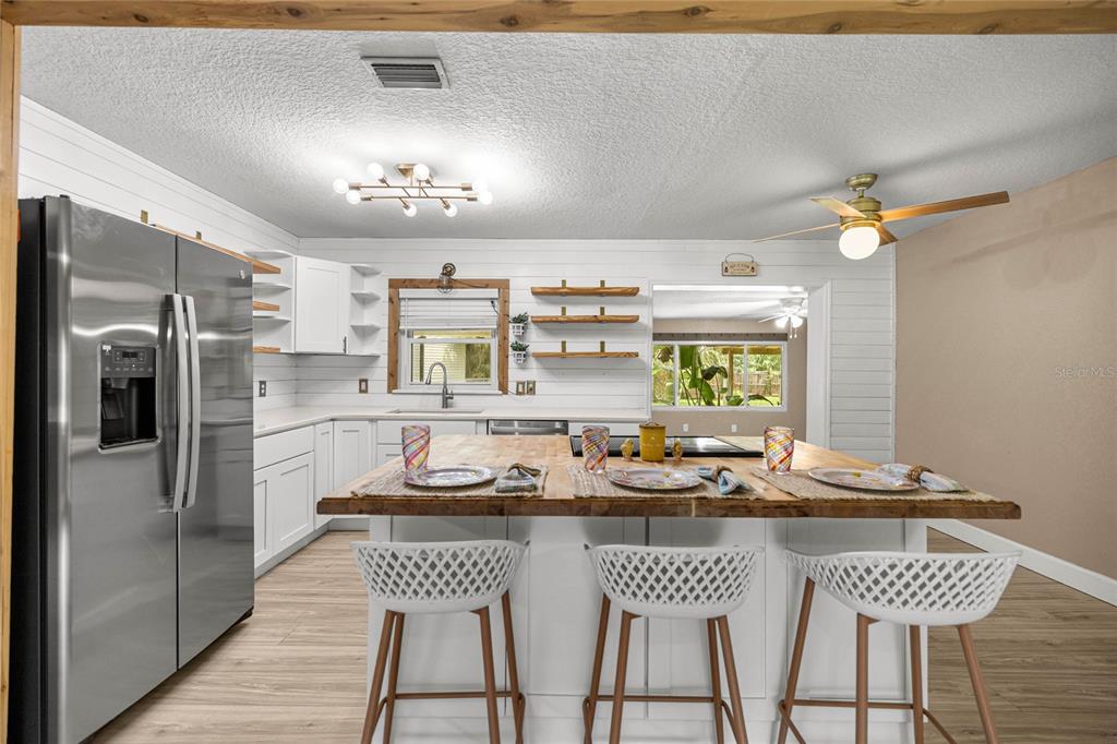 A kitchen features a wooden island, white cabinetry, open shelving, and a stainless steel refrigerator — 2021 NW 13TH AVENUE, CRYSTAL RIVER, FL