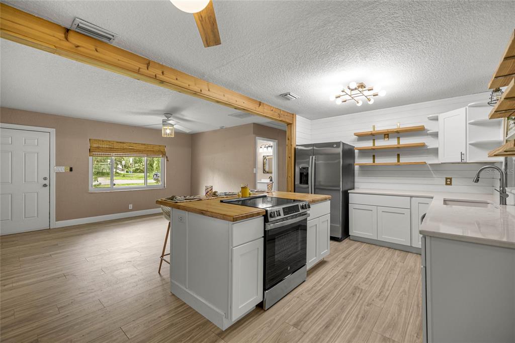 A kitchen with white cabinets, a wooden island, and open shelving opens into a living area — 2021 NW 13TH AVENUE, CRYSTAL RIVER, FL