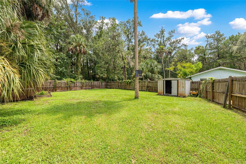 A grassy backyard features a wooden fence, a metal storage shed, and mature trees — 2021 NW 13TH AVENUE, CRYSTAL RIVER, FL