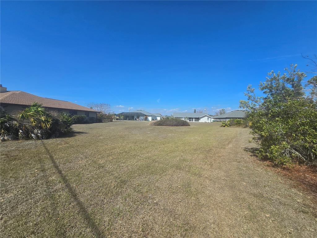 A wide, grassy vacant lot is surrounded by residential houses under a clear blue sky — 154 SANTOS DRIVE, PUNTA GORDA, FL
