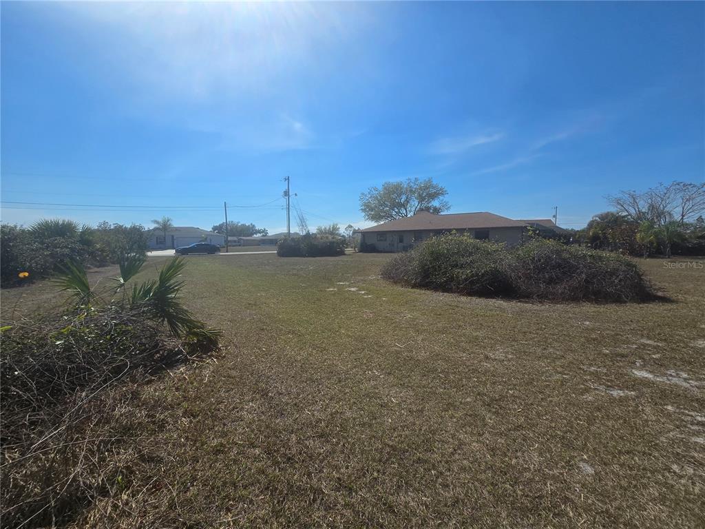 A large, grassy vacant lot features scattered brush and a house in the background — 154 SANTOS DRIVE, PUNTA GORDA, FL