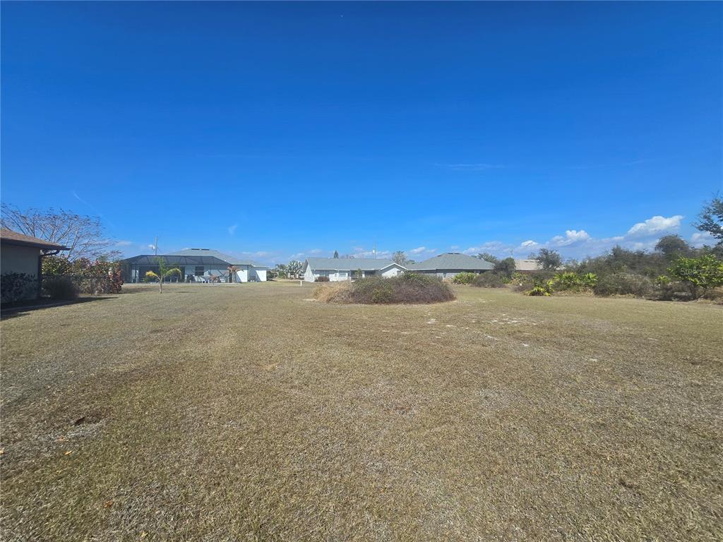 A wide, grassy vacant lot under a clear blue sky with neighboring houses visible — 154 SANTOS DRIVE, PUNTA GORDA, FL
