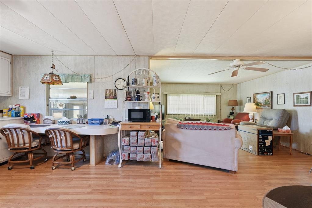 A living room and dining area with wood-look flooring, wood-paneled walls, and a ceiling fan — 64 RACHEL DRIVE, TARPON SPRINGS, FL