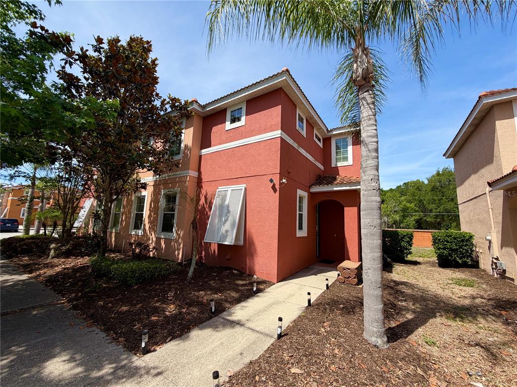 A two-story stucco townhouse with a red exterior, a palm tree, and a front walkway — 720 LAS FUENTES DRIVE, KISSIMMEE, FL