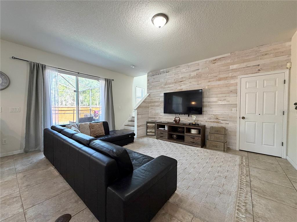 A living room features a black sectional sofa, a television mounted on a wood-paneled wall — 720 LAS FUENTES DRIVE, KISSIMMEE, FL