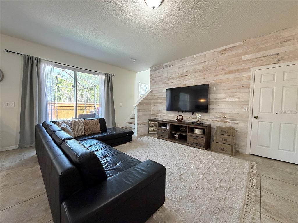 A living room features a black sectional sofa, a wood-paneled accent wall, and a television — 720 LAS FUENTES DRIVE, KISSIMMEE, FL
