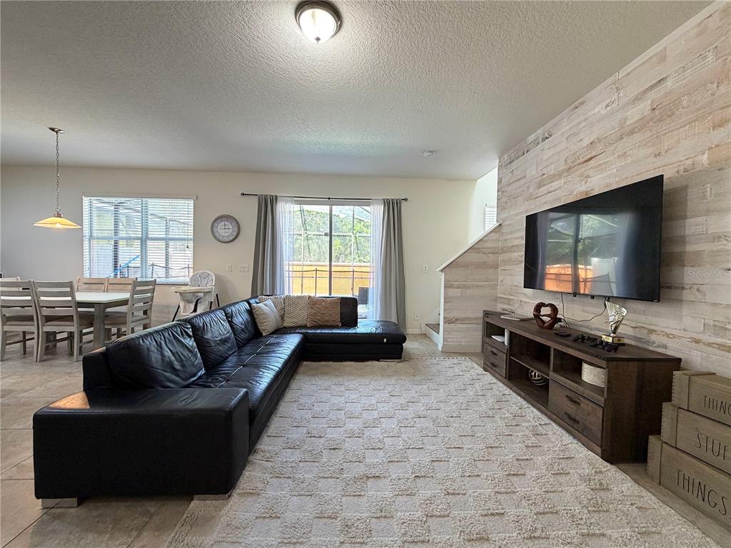 A living room features a black sectional sofa, a television on a wood-paneled wall, and dining area — 720 LAS FUENTES DRIVE, KISSIMMEE, FL